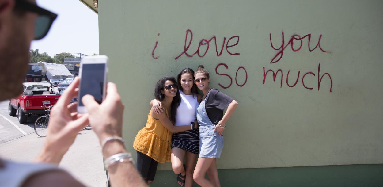 Girls posing at I Love You So Much Mural while friend takes photo