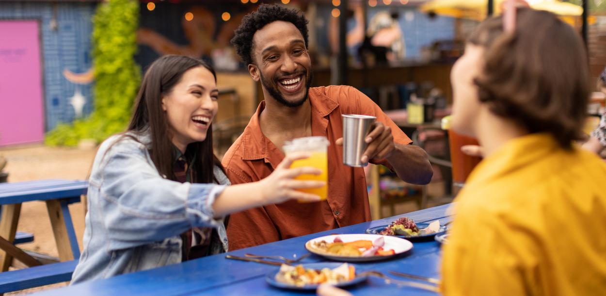 Two women and a man cheering drinks over plates of tacos.