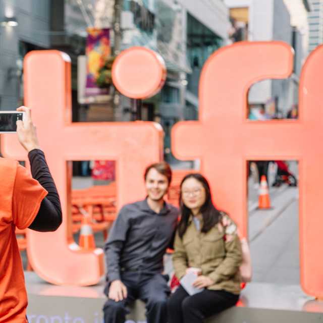 A TIFF Volunteer takes a photo of a couple in front of the TIFF sign