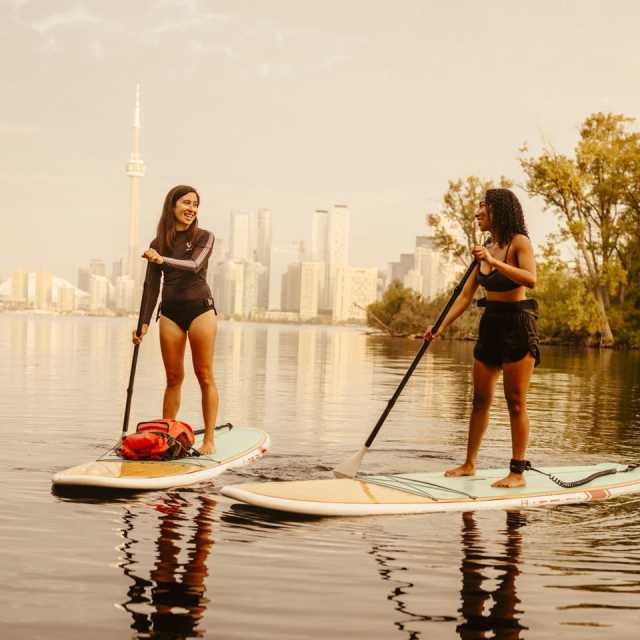 Two people on paddle boards on Lake Ontario, with the Toronto skyline in the background