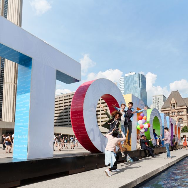 A group of tourists pose at the Toronto sign at Nathan Philips Square