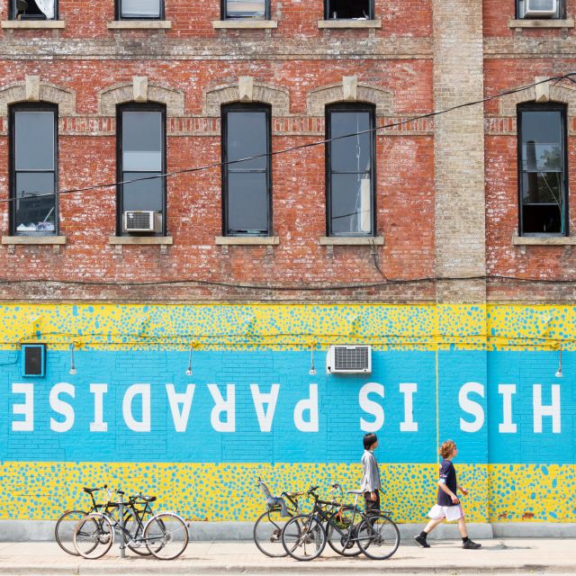 People walk by a wall mural that reads "This is Paradise" in Toronto's Queen Street West neighbourhood