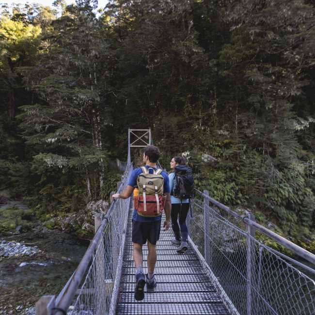 People crossing bridge into native bush at the start of the Routeburn Track