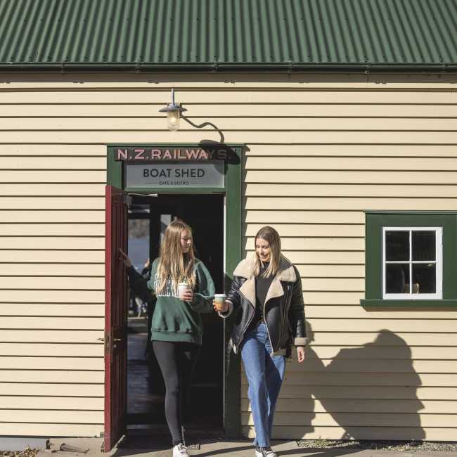 Two people walking out of the Boat Shed Café with keep cups