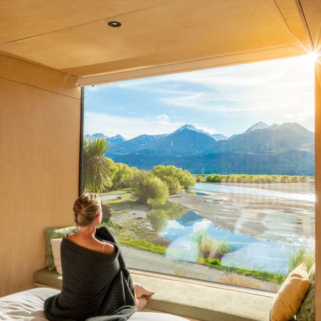 Woman looking out a huge window with view of mountains and lake at Kinloch Wilderness Retreat