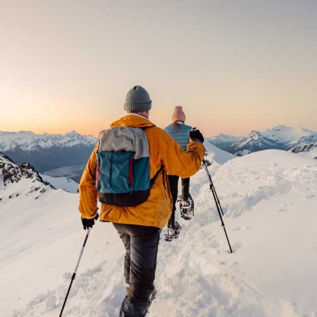 Point of view image with two people snow shoeing surrounded by snow covered mountains