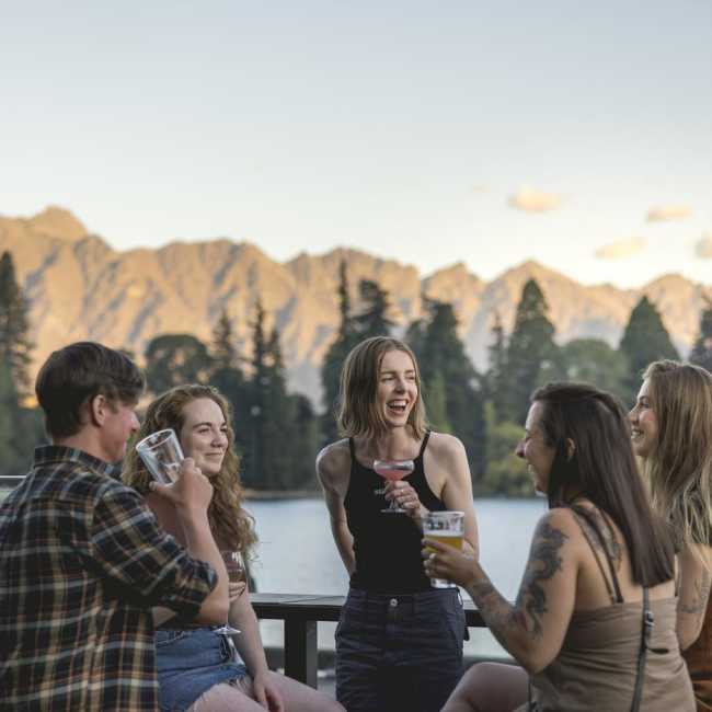 Friends laughing together with a drink in hand with lake and mountains in the background