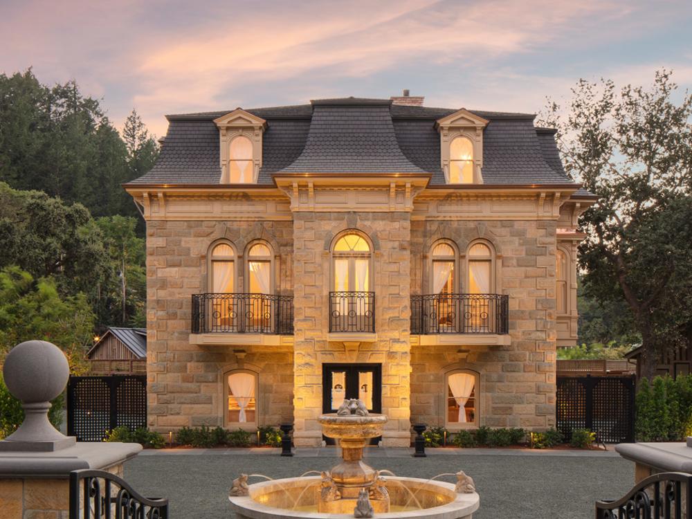 The elegant Francis House mansion has a gabled roof, glowing windows, intricate balconies, and a central fountain, surrounded by lush greenery.