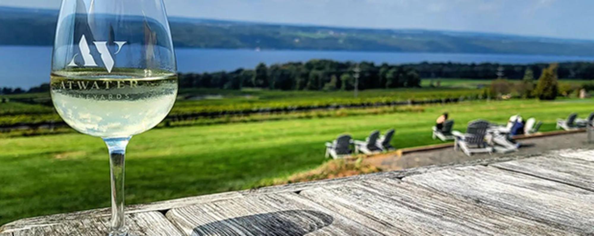 A glass on wine sitting on a wooden boardwalk with views of Seneca Lake in the background
