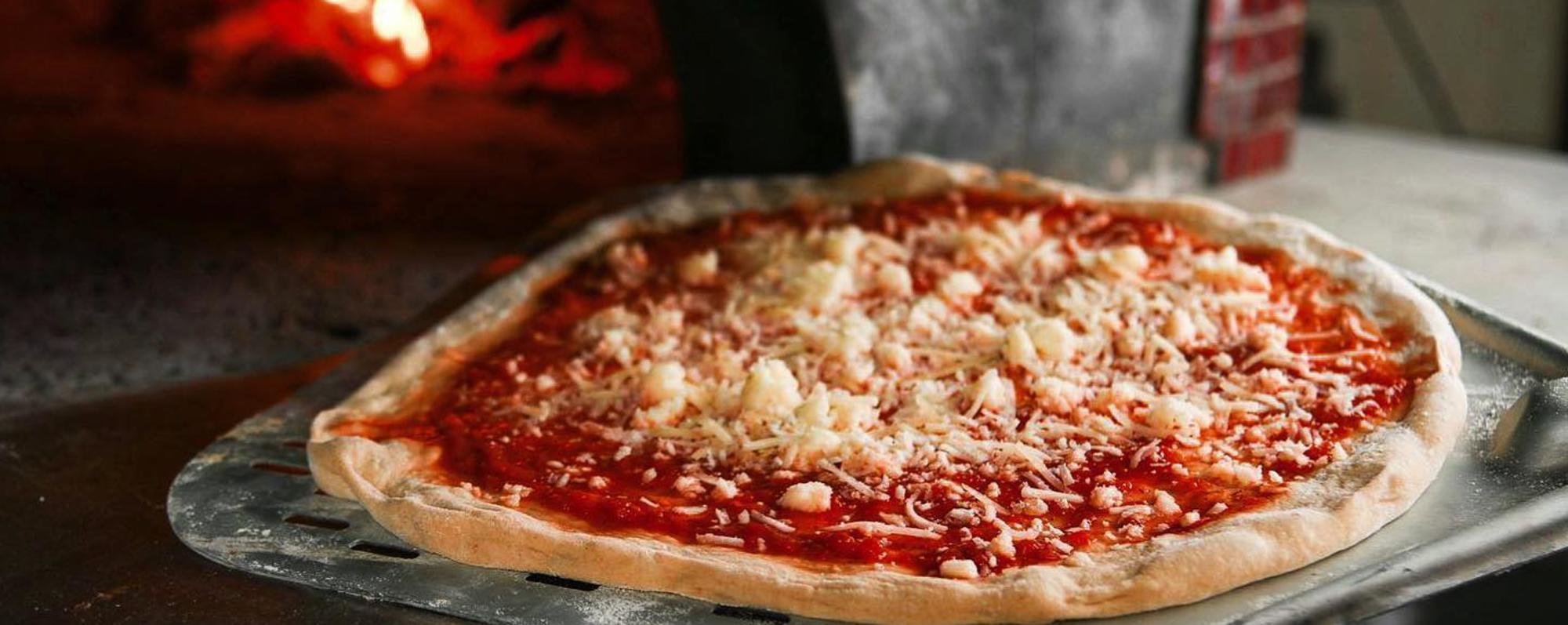 A pizza topped with cheese and tomato sauce being transferred on a peel into a wood-fired oven.