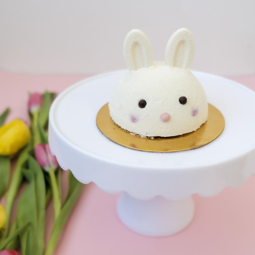 Bunny-shaped tart sitting on a white cake pedestal next to a group of tulips.