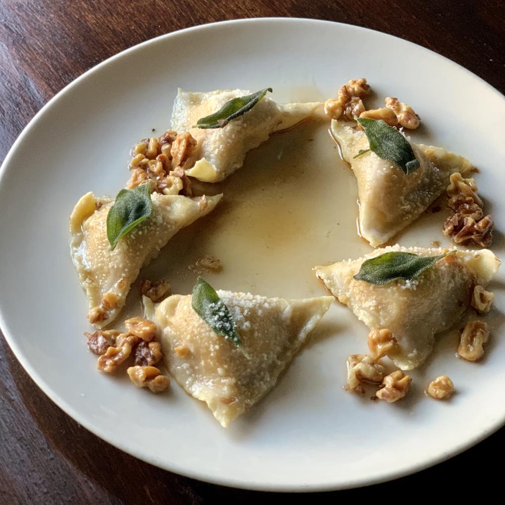 Fried ravioli topped with crispy sage pieces on a white plate.