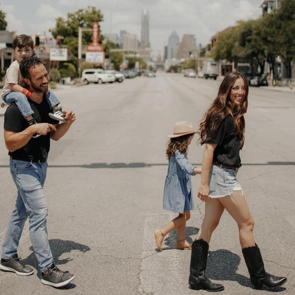 Family of four strolling across a crosswalk on South Congress Avenue with Texas State Capitol and Austin Motel in the background.