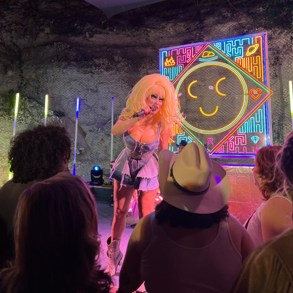 Drag queen on outdoor stage at Cheer Up Charlies with neon art in the background