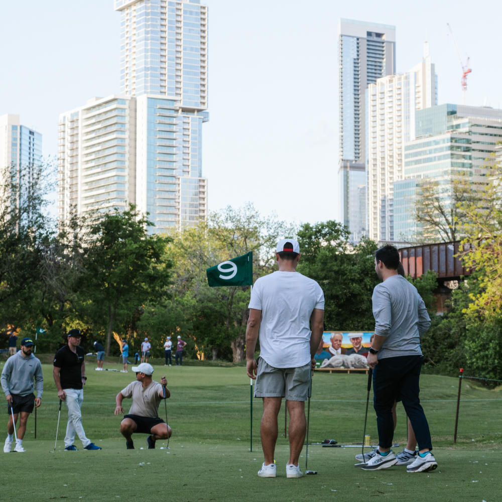 Five guys around a golf hole, trying to line up a putt.