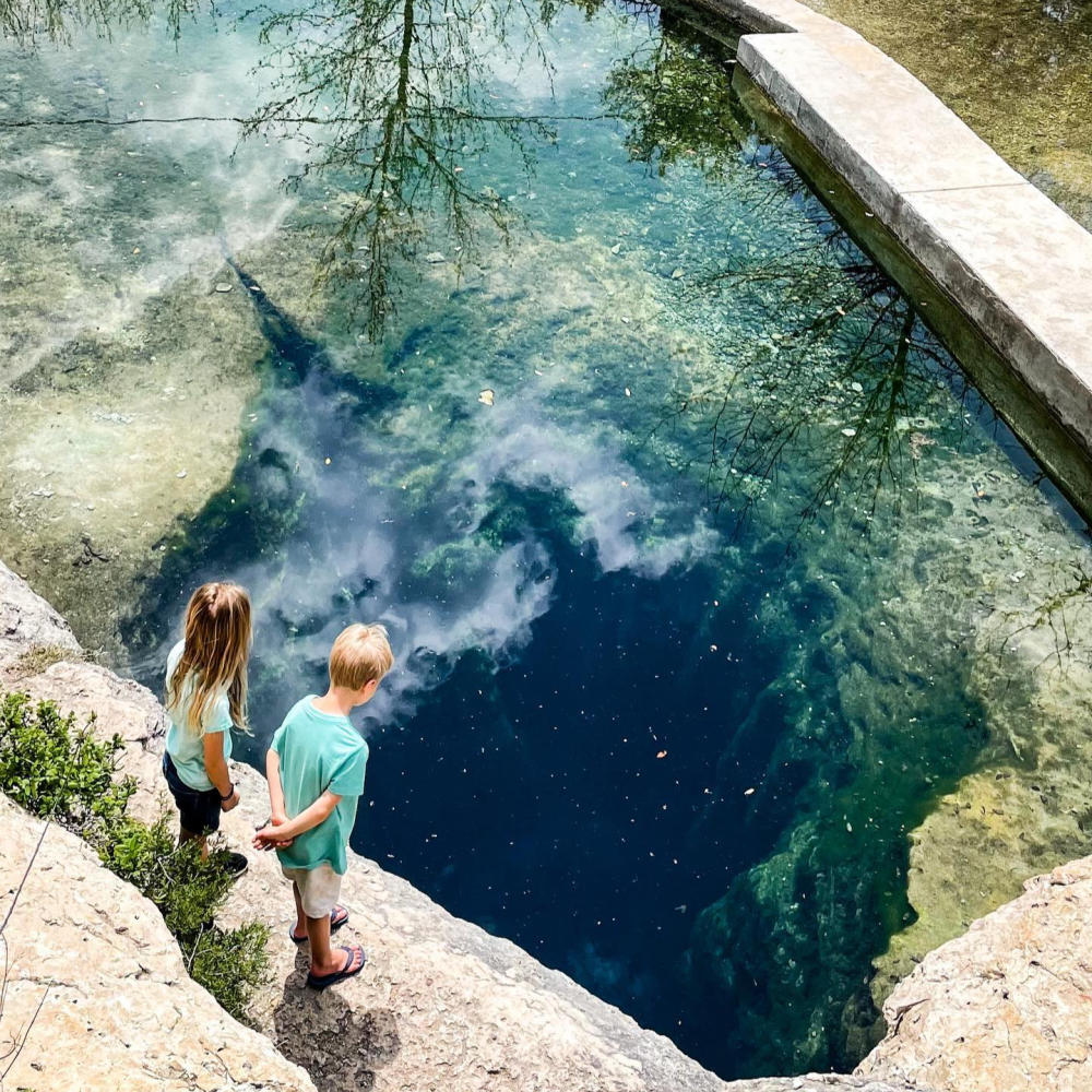 Two children looking at Jacob's Well from a viewing area above the water.