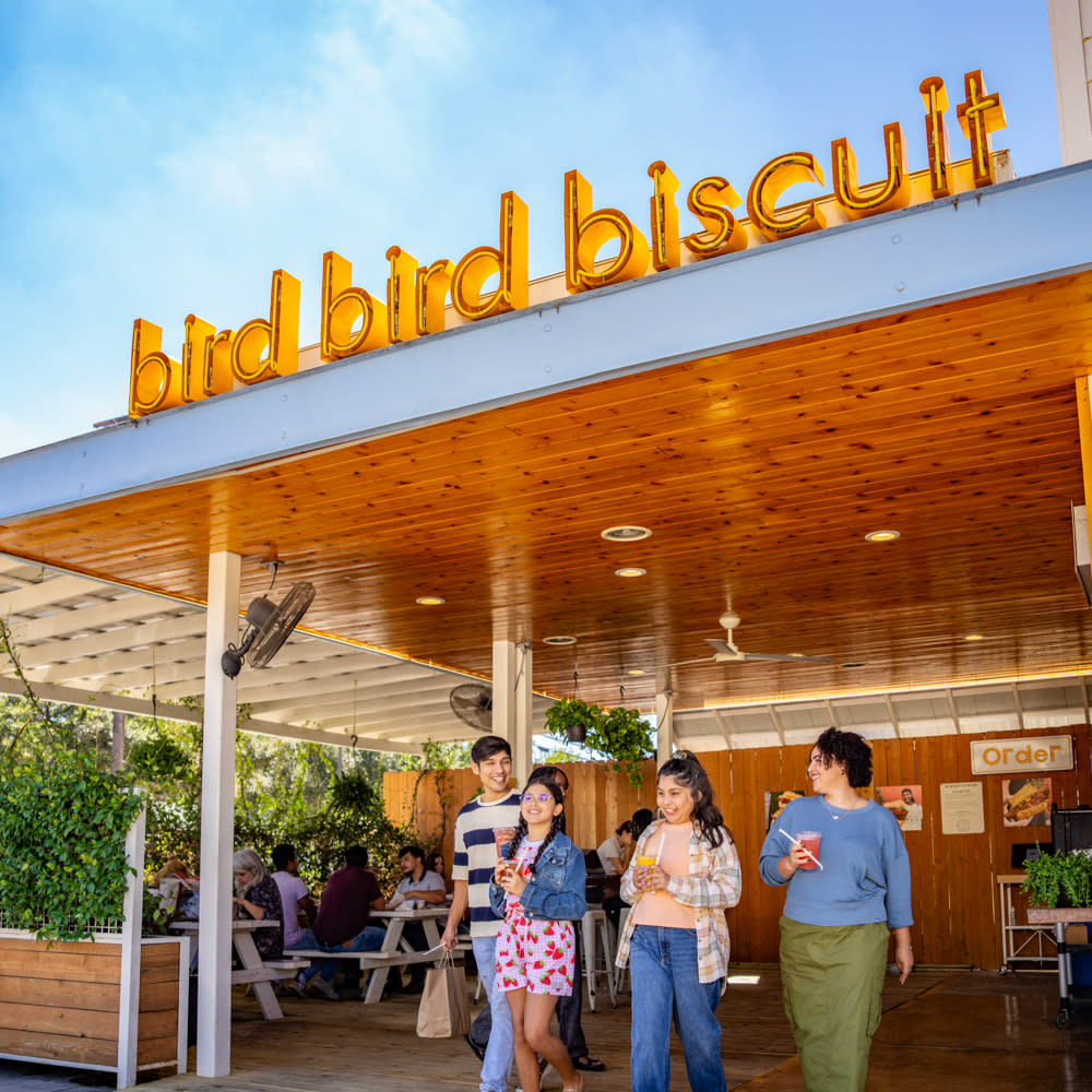 Image of a group of four men and women walking out of a restaurant with the sign above them on the wall reading "Bird Bird Biscuit".