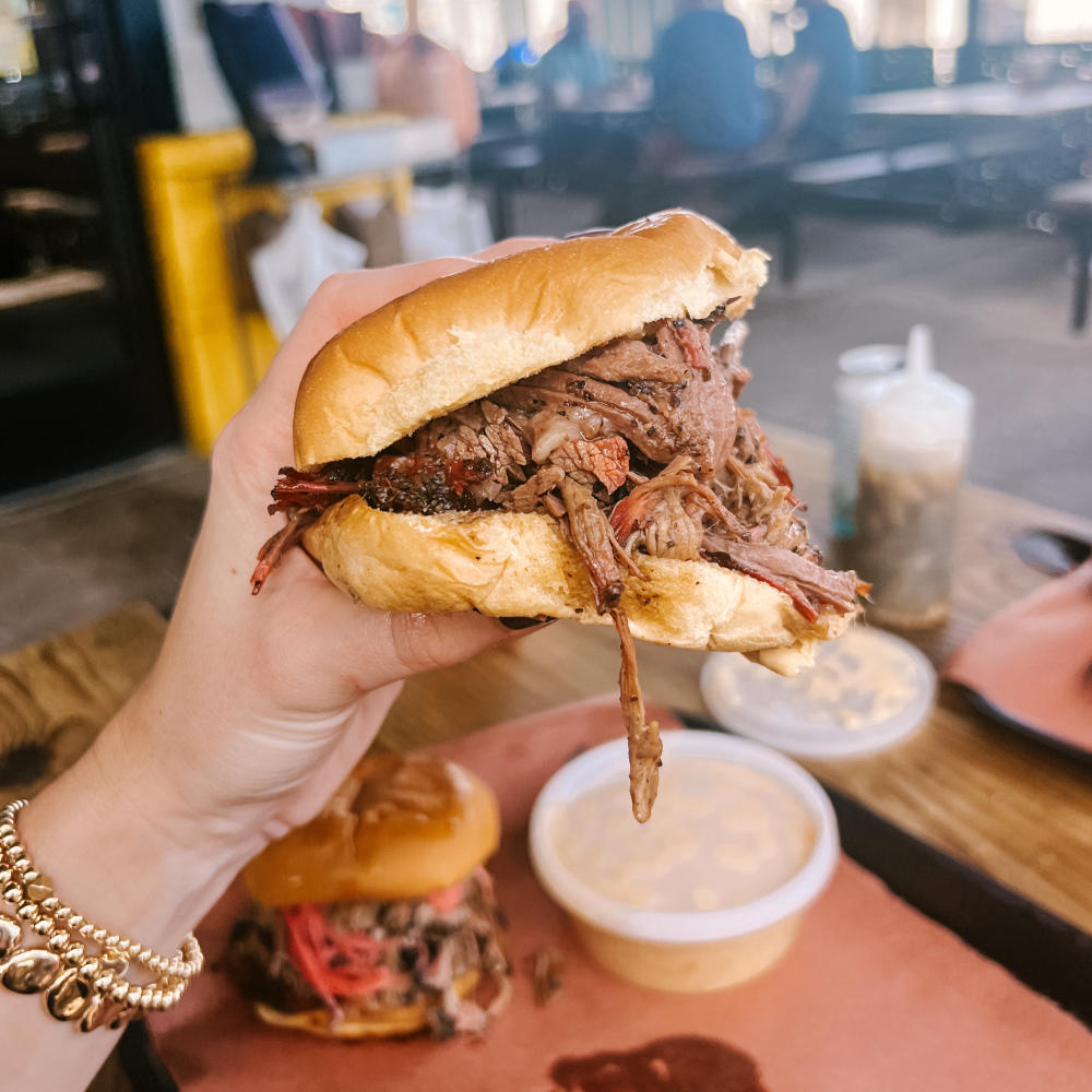 Hand holding a large barbecue sandwich close to the camera.