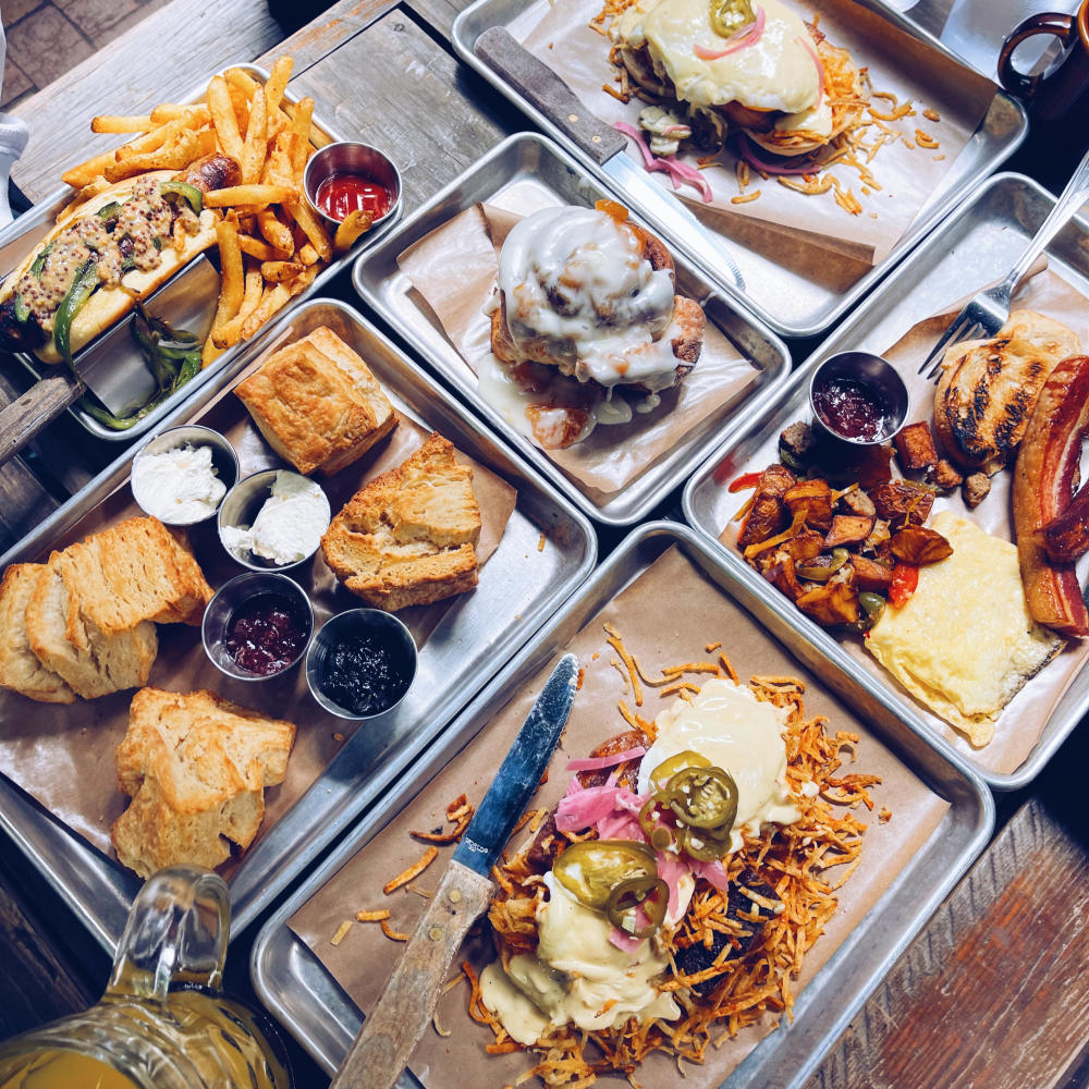 Brunch spread of biscuits, hashbrowns, sausages, cinnamon rolls and bacon on silver quarter sheet trays.