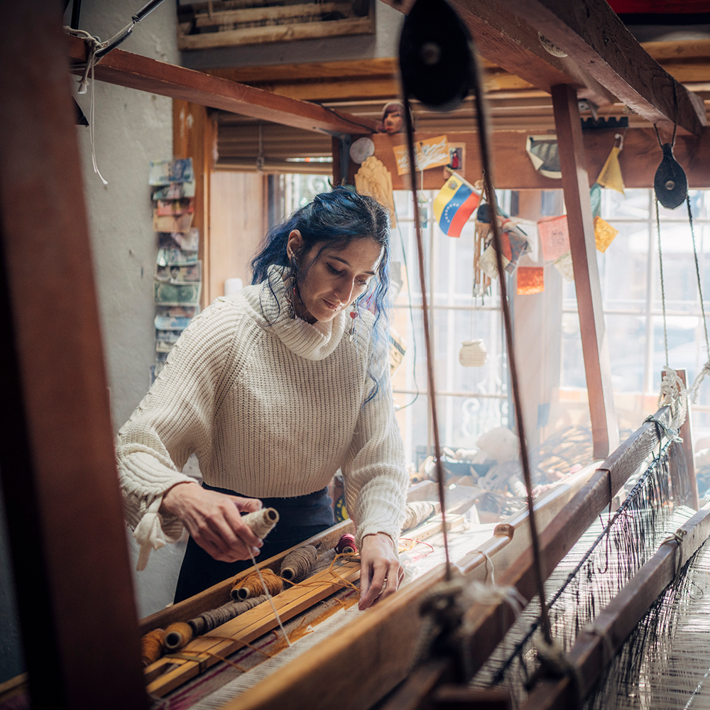Person working at a large wooden loom inside a workshop.