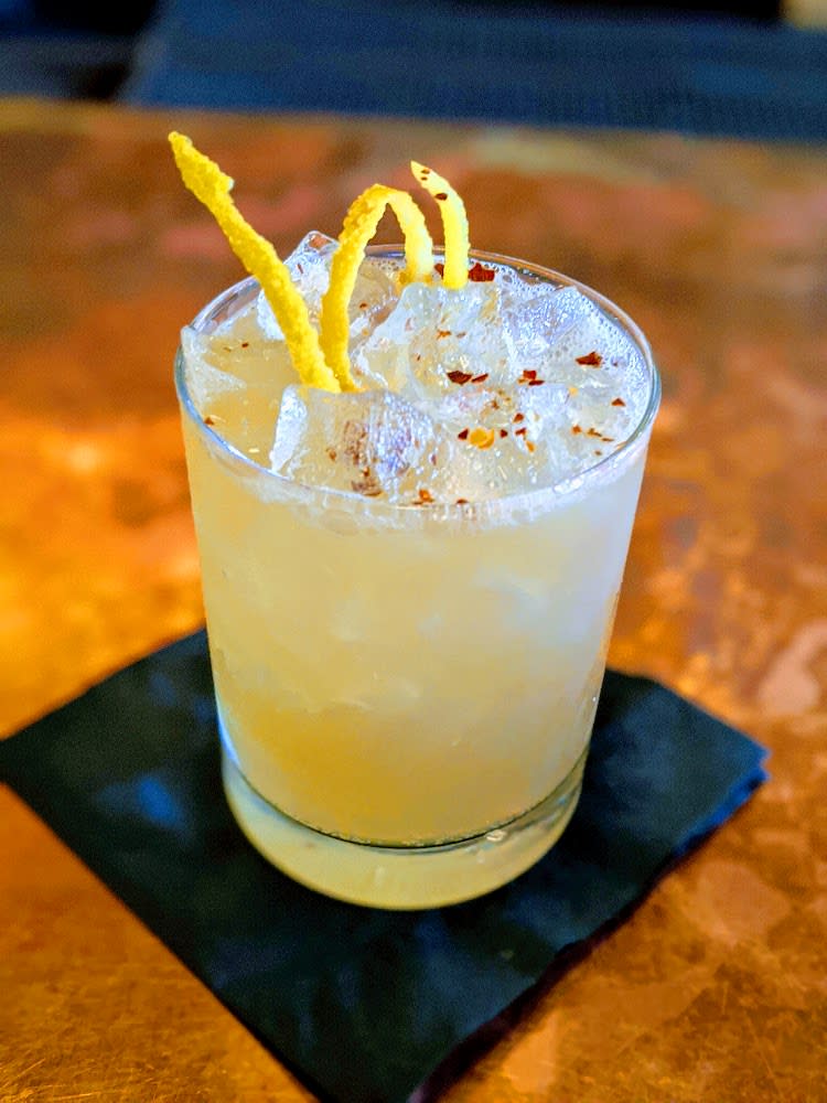 A short glass filled with a light yellow lemon cocktail with cinnamon and a twist of lemon on top at OKBB