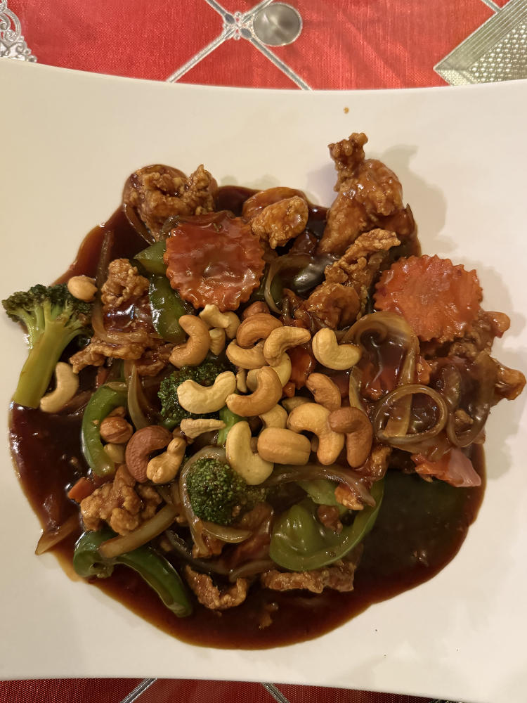 The Bangkok Chicken featuring crispy chicken, vegetables, and cashews in a glazed sauce is on a white plate at Bangkok Flavor.
