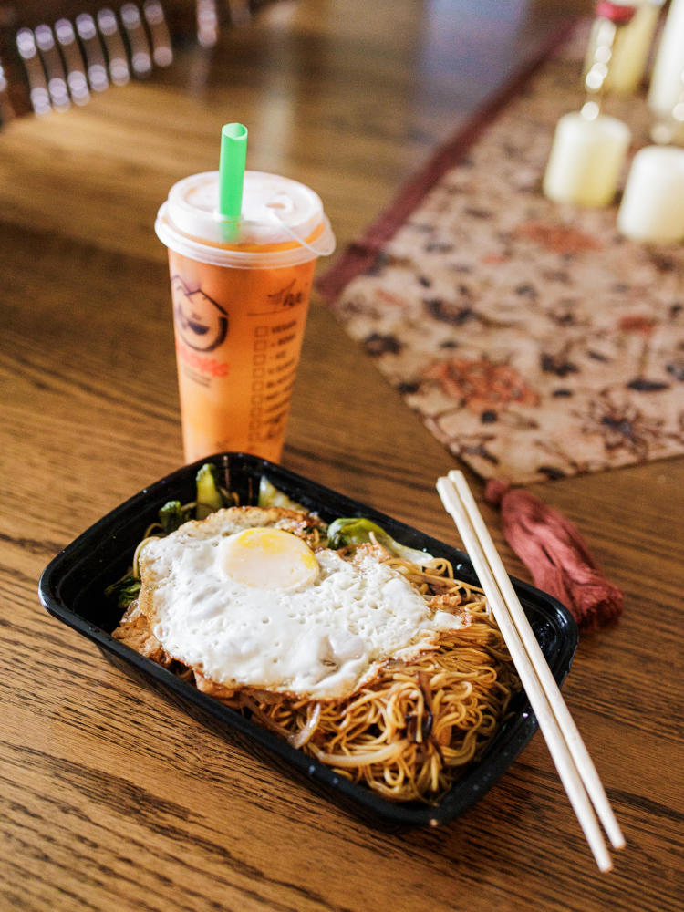 A pink boba tea sits next to a stir-fry noodle dish at Cravings Corner.