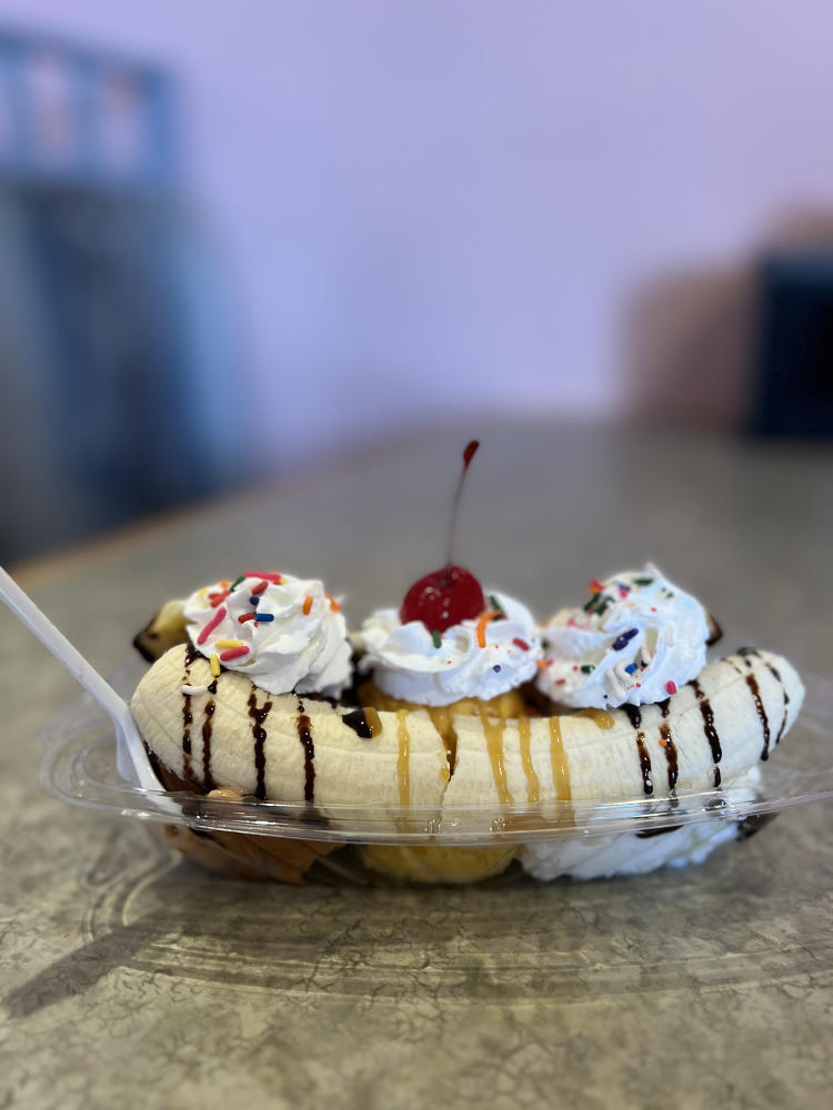 Monarca's banana split sundae features three different flavors of ice cream between a split banana, topped with caramel and chocolate syrup, with whipped cream and sprinkles.