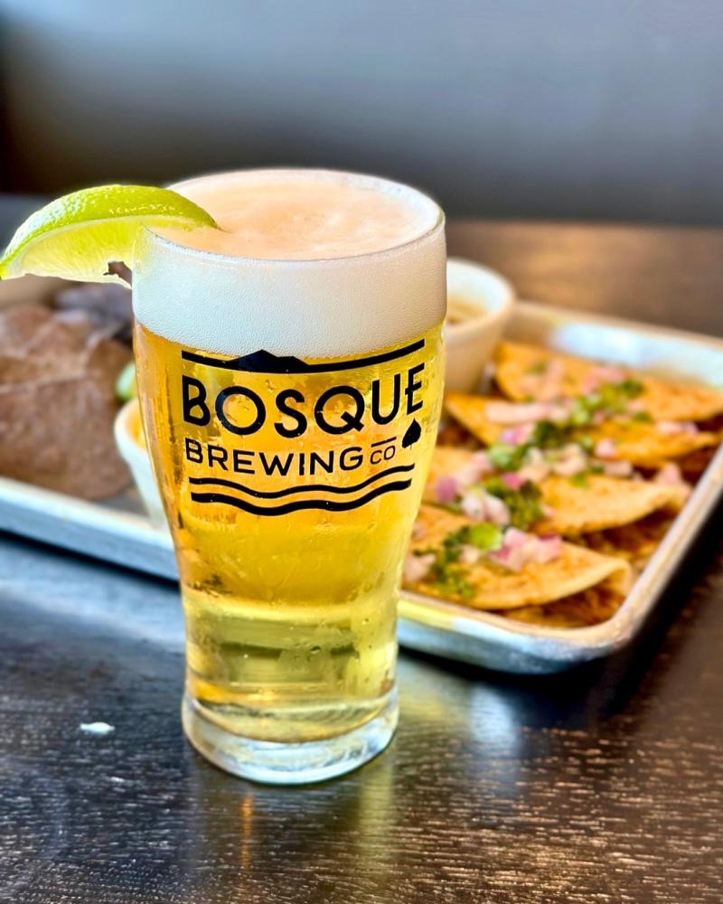 A glass of beer from Bosque Brewing Co. sits in front of a plate of tacos.