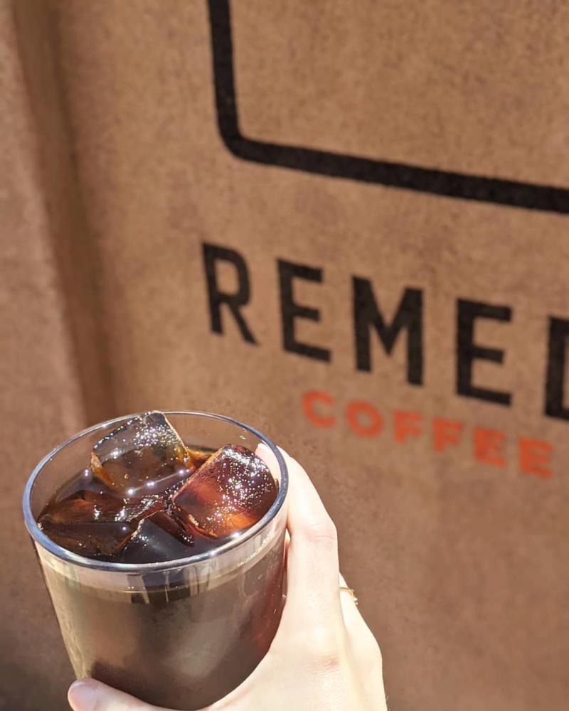 Someone holds a cup of cold brew in front of the Remedy Coffee sign.