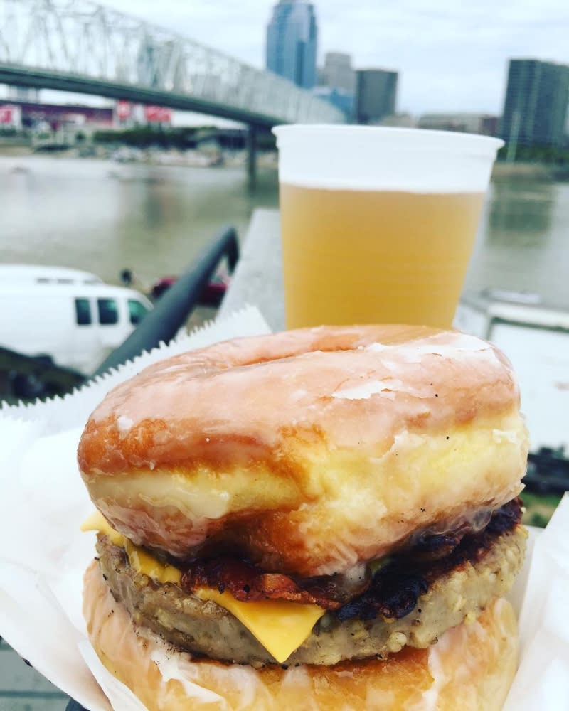 Goetta donut sandwich with a plastic glass filled with beer and a bridge in the background