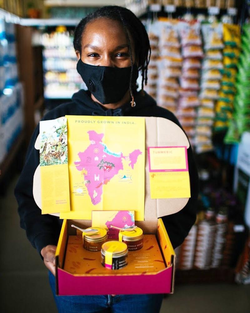 Woman holding a box of products sourced from India at the West Oakland Mandela Grocery COOP