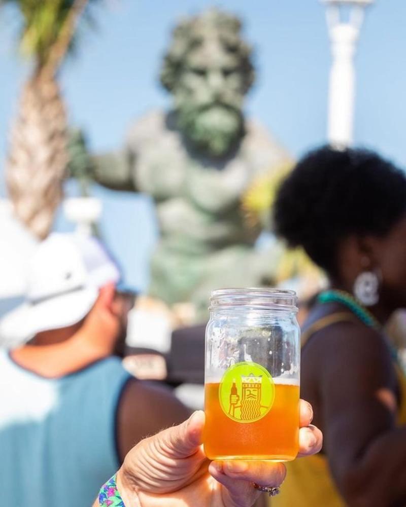 person holding glass of craft beer with King Neptune statue in the background
