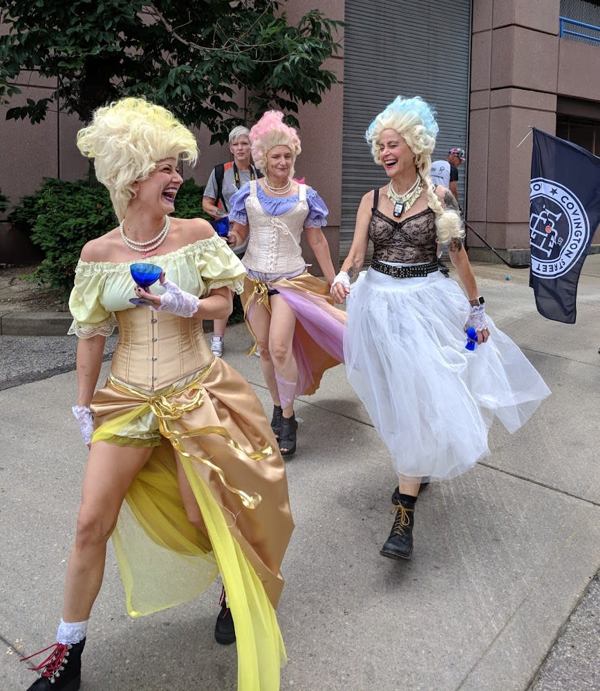 Three drag queens dressed in 18th century dresses and wigs