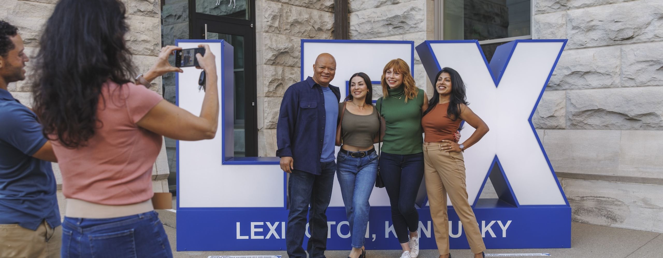 Group of people getting their picture taken in front of a LEX sign.