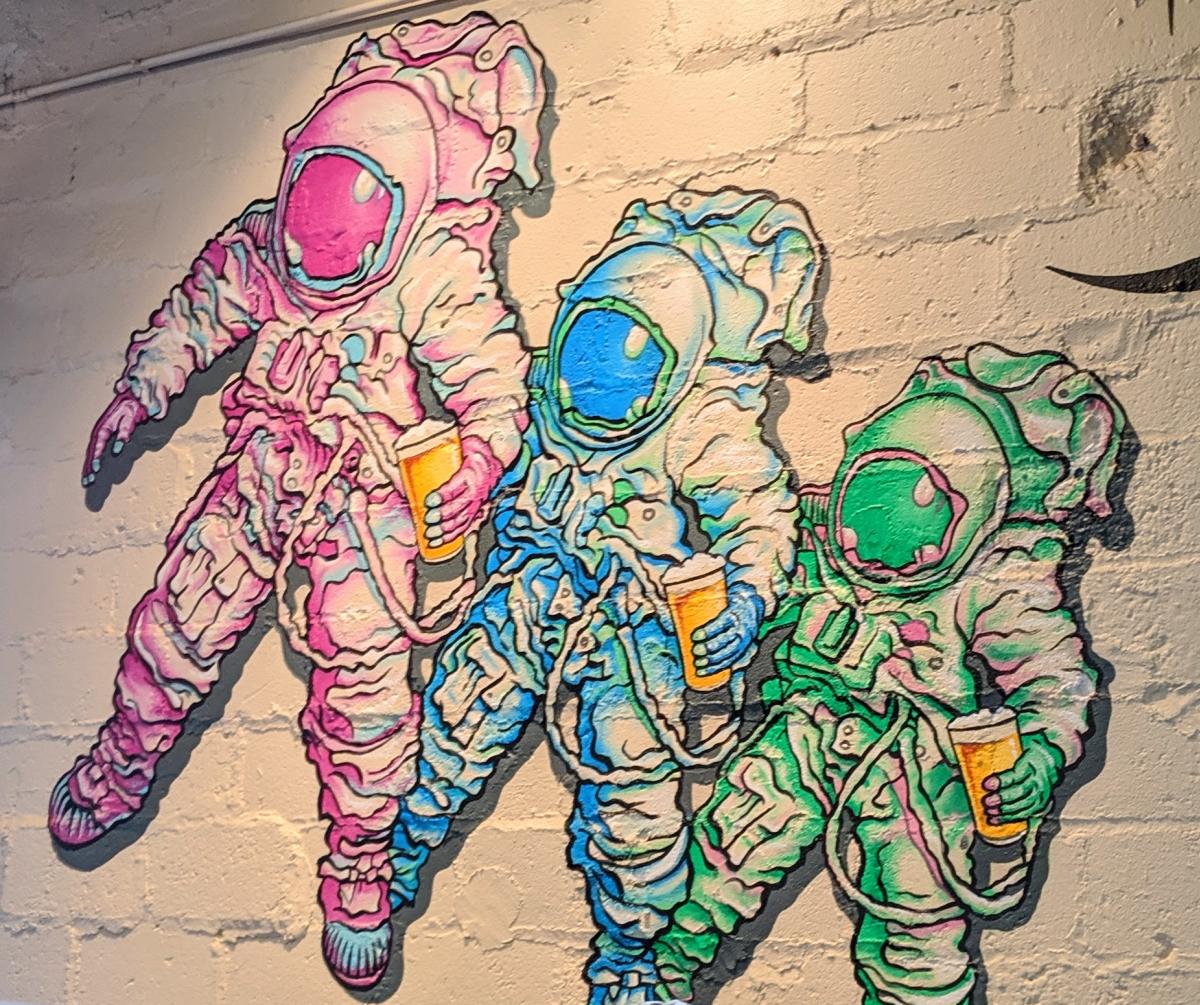 A mural of three astronauts, one pink, one blue, and one green, all holding pints of beer, at Darkness Brewery in Bellevue, Ky.