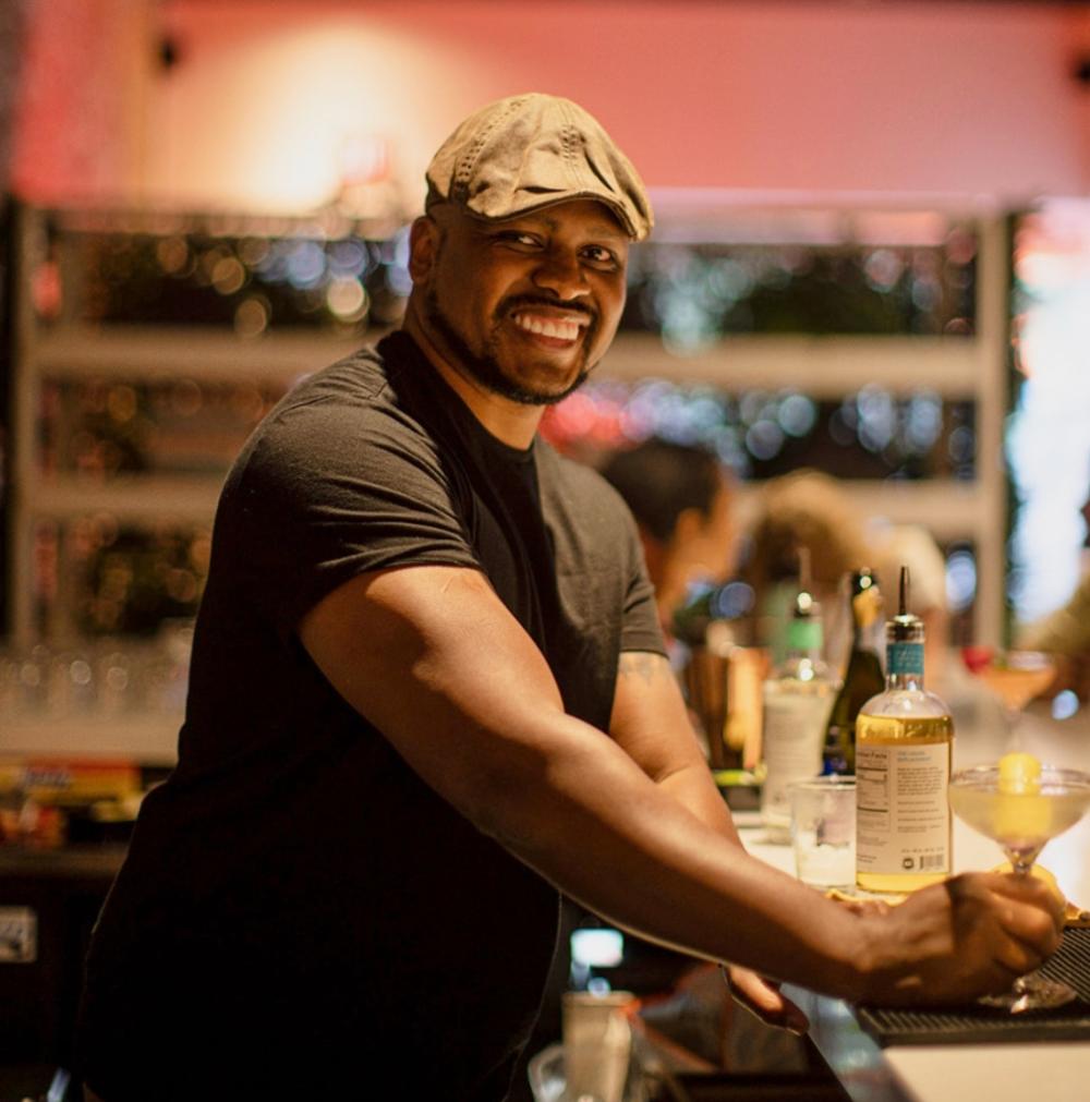 Owner of Sans Bar, Chris Marshall standing behind the bar with an n/a cocktail.