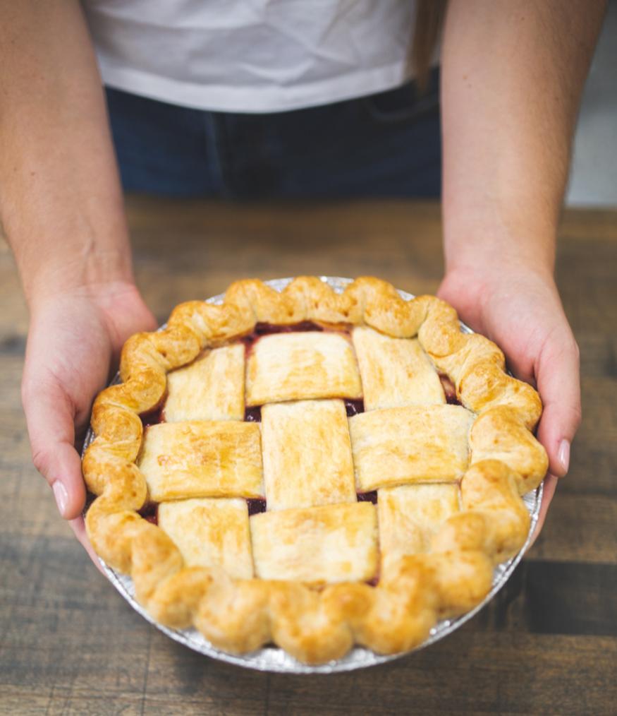 hands holding a large lattice-work crust topped pie