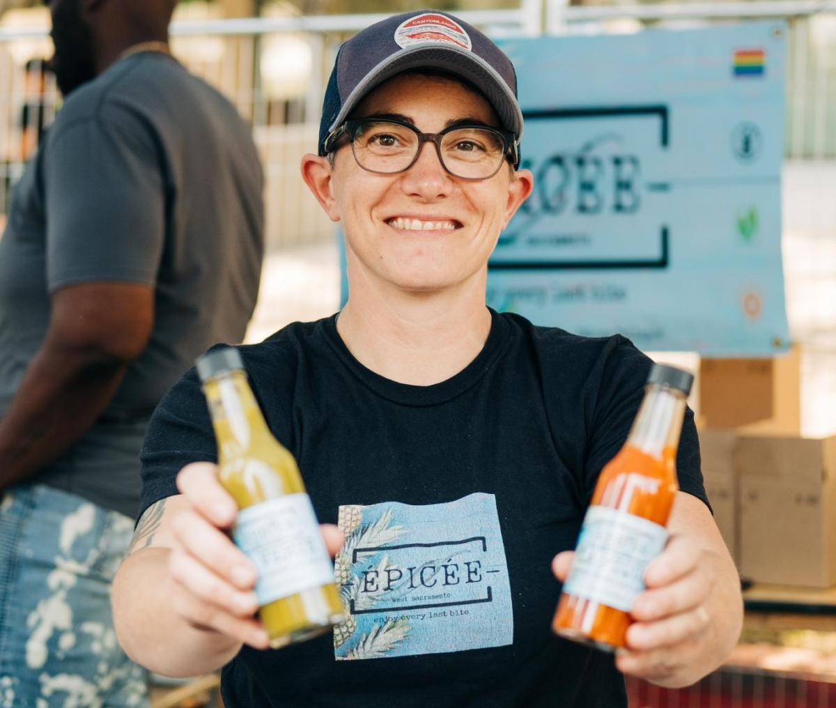 A vendor at a street festival showing off two bottles of hot sauce