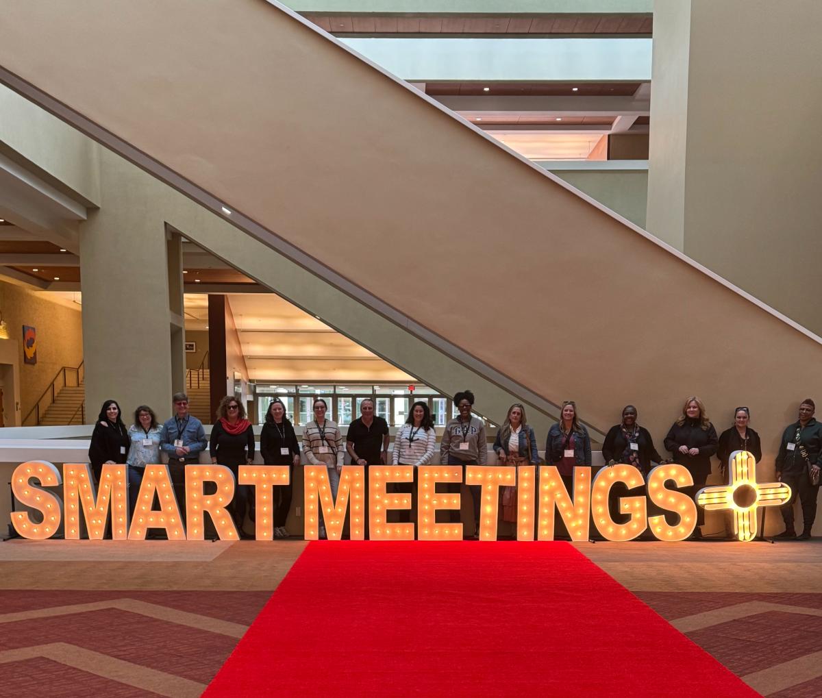 Group of meeting planners and hospitality professionals posting in front of letters spelling "Smart Meetings"
