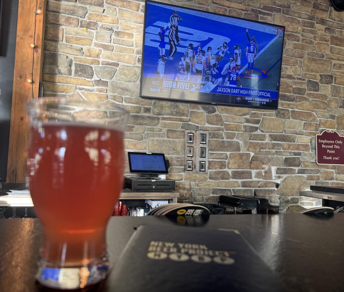 Glass of beer at New York Beer Project, Victor NY at the bar with football on the television screen