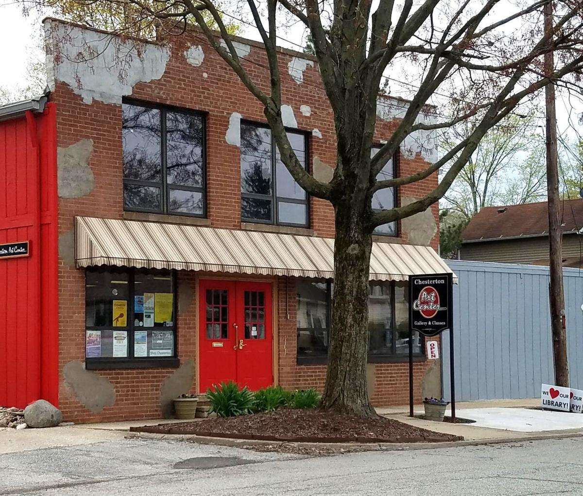 A brick building with a bright red door. A large tree sits in front of the building.