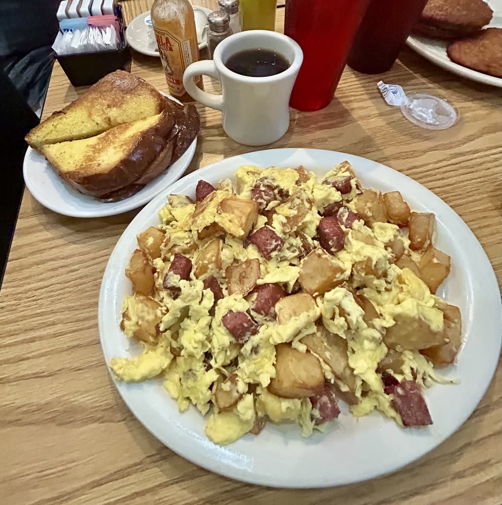 A hearty breakfast plate with scrambled eggs, diced potatoes, and chunks of corned beef, served with a side of thick-cut toast and a cup of coffee.