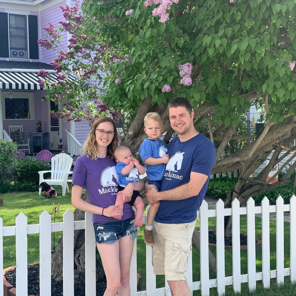 A couple with two children stand by a white picket fence in front of a cottage on Mackinac Island
