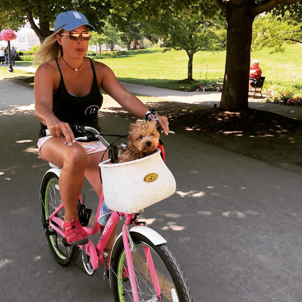 Woman Riding Bicycle with Dog Sitting in Basket in Downtown Mackinac