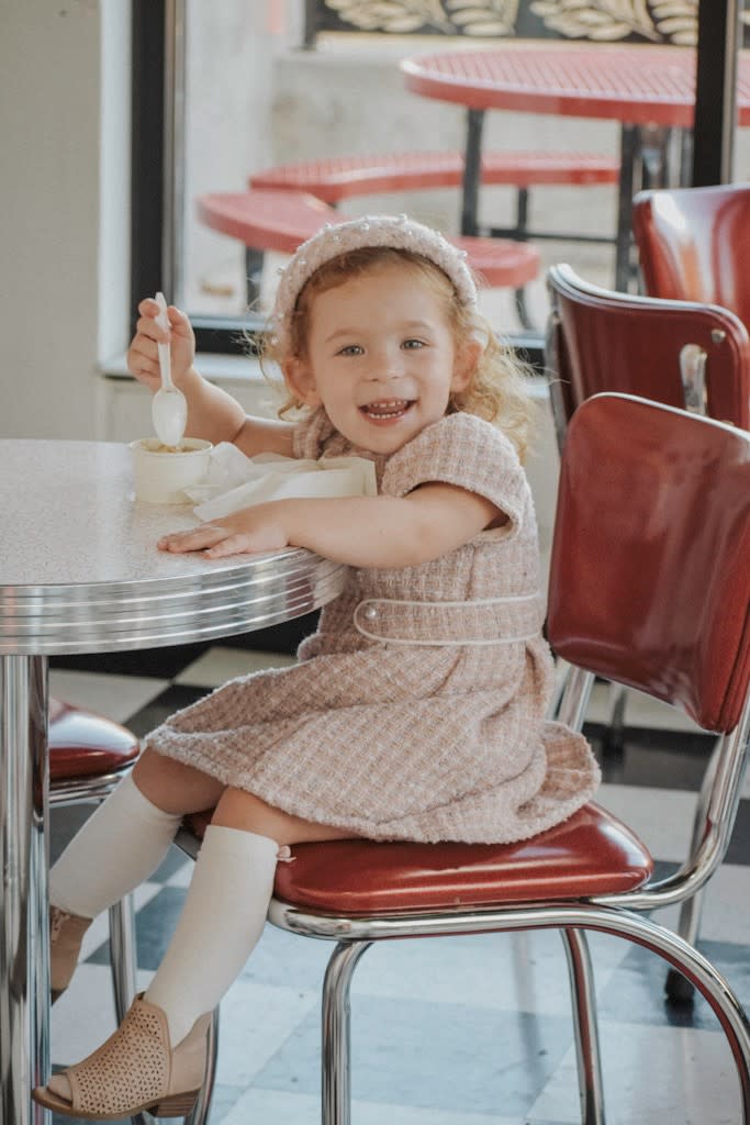 Little girl sits in chair in ice cream Shoppe, eating ice cream and smiling at camera