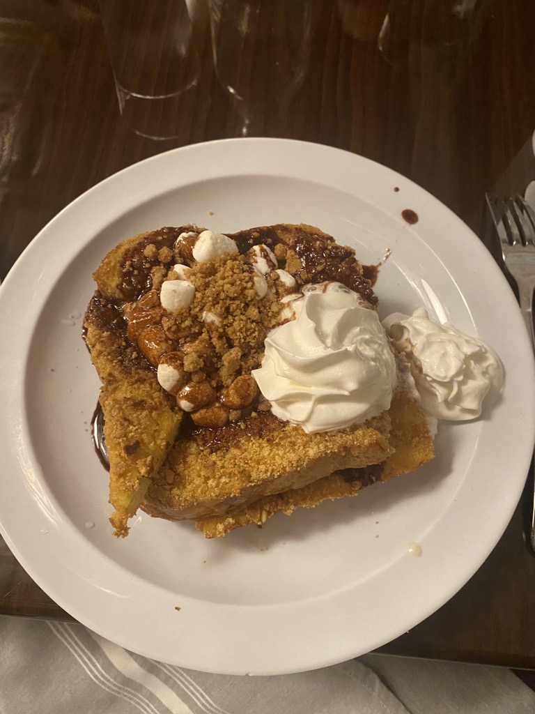 Image is of 4 pieces of French toast with marshmallows, graham cracker bits and chocolate sauce.