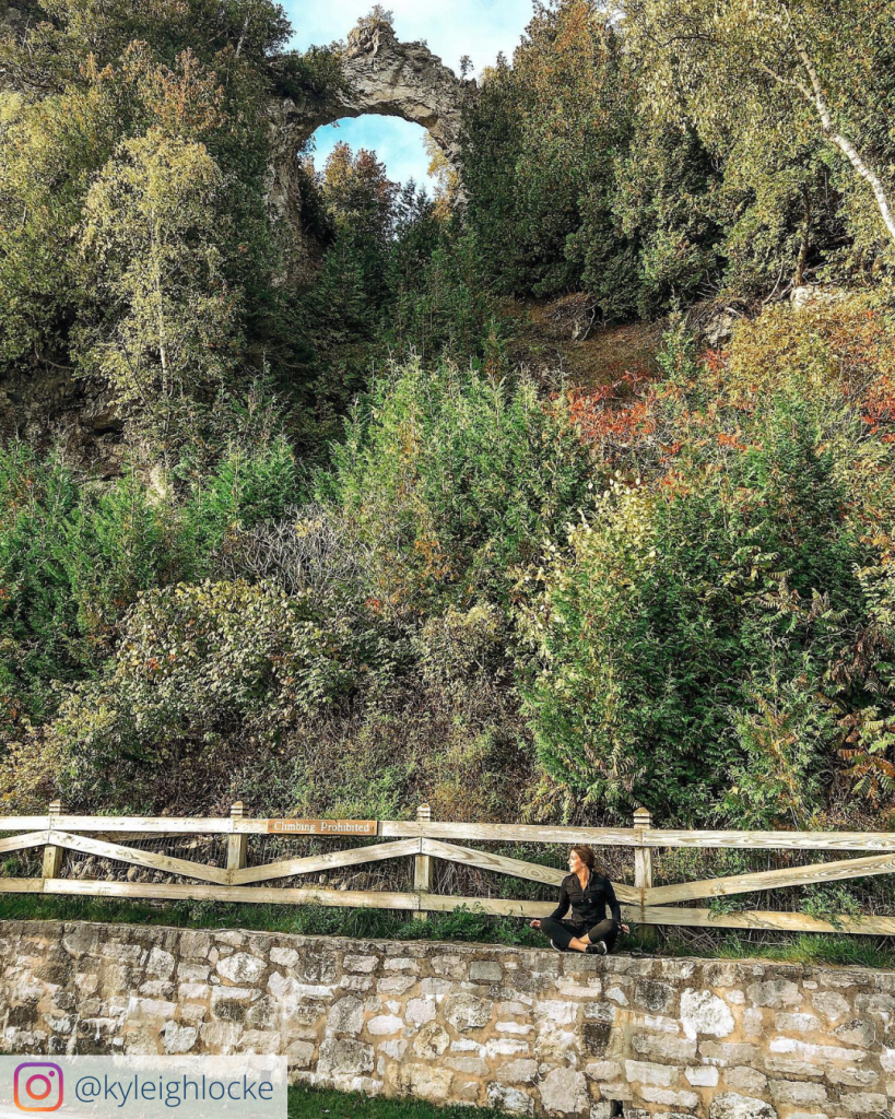 A woman sits on a brick wall beneath Arch Rock during a run around Mackinac Island.