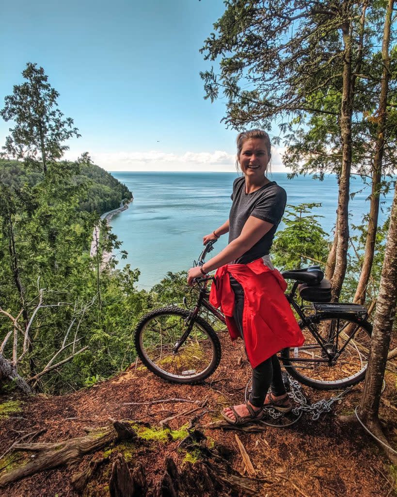Woman with Bike Smiling for Camera Overlooking View of Waters Around Mackinac