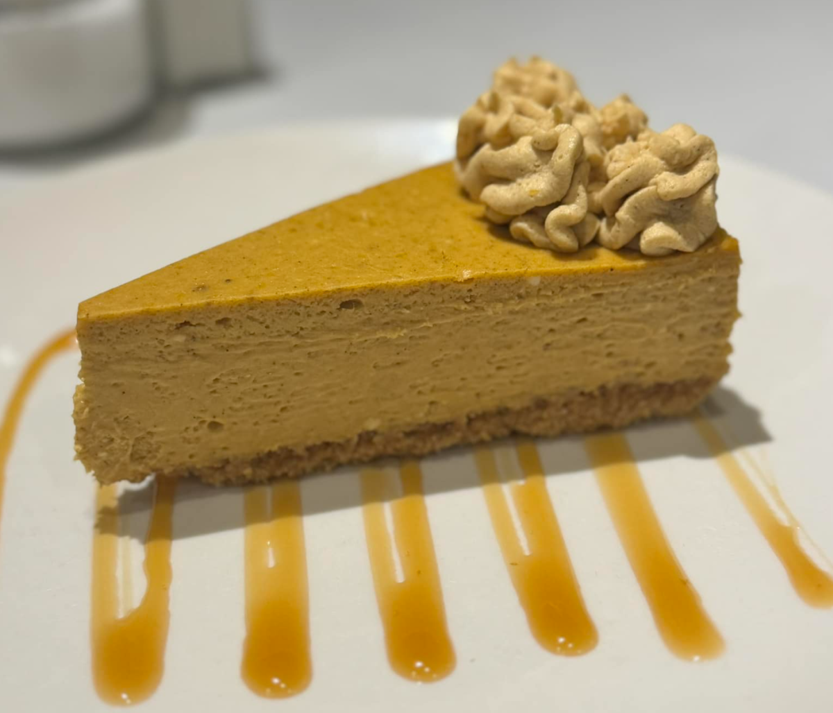 A slice of pumpkin cheese cake on a plate with icing swirled on top